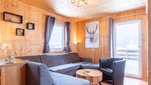 A cozy cabin interior with a gray sofa, a wooden coffee table, and a mounted deer head artwork.