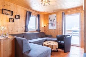Interior acogedor de una cabaña con un sofá gris, una mesa de centro de madera y una obra de arte con un ciervo montado.