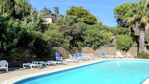 A swimming pool with lounge chairs and a stone wall. - Holiday Home in Bormes-les-mimosas Near Sea (Bormes-Les-Mimosas)