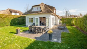 Een huis met rieten dak, een eethoek met buitenmeubilair en een keurig onderhouden tuin.