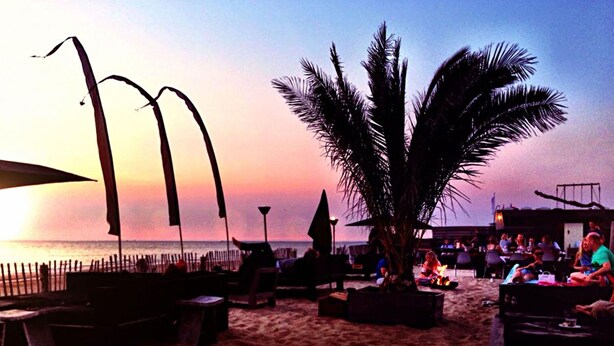 A beachside lounge with outdoor seating, a fire pit, and a view of the ocean at sunset. - Modified, Modern Lodge Near the Beach (Zandvoort)