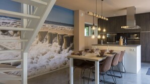 Una cucina moderna con isola centrale, illuminazione a sospensione e un murale a tema costiero.
