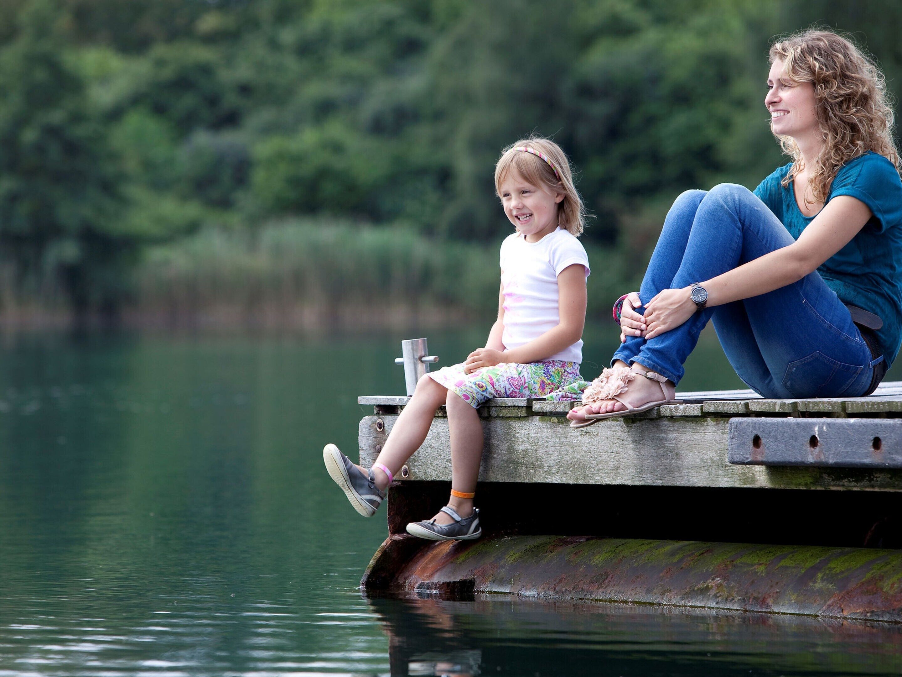 Two people sitting on a wooden dock by a calm body of water.