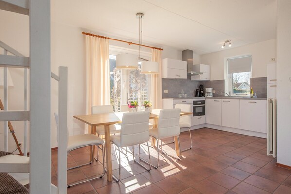 A modern kitchen with white cabinets, a dining table with chairs, and a window with curtains. - Detached Well-kept Villa With Garden, Near the Beach (Kamperland)