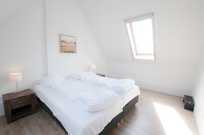 A bedroom with a bed, a nightstand, a lamp, a picture on the wall, and a window.