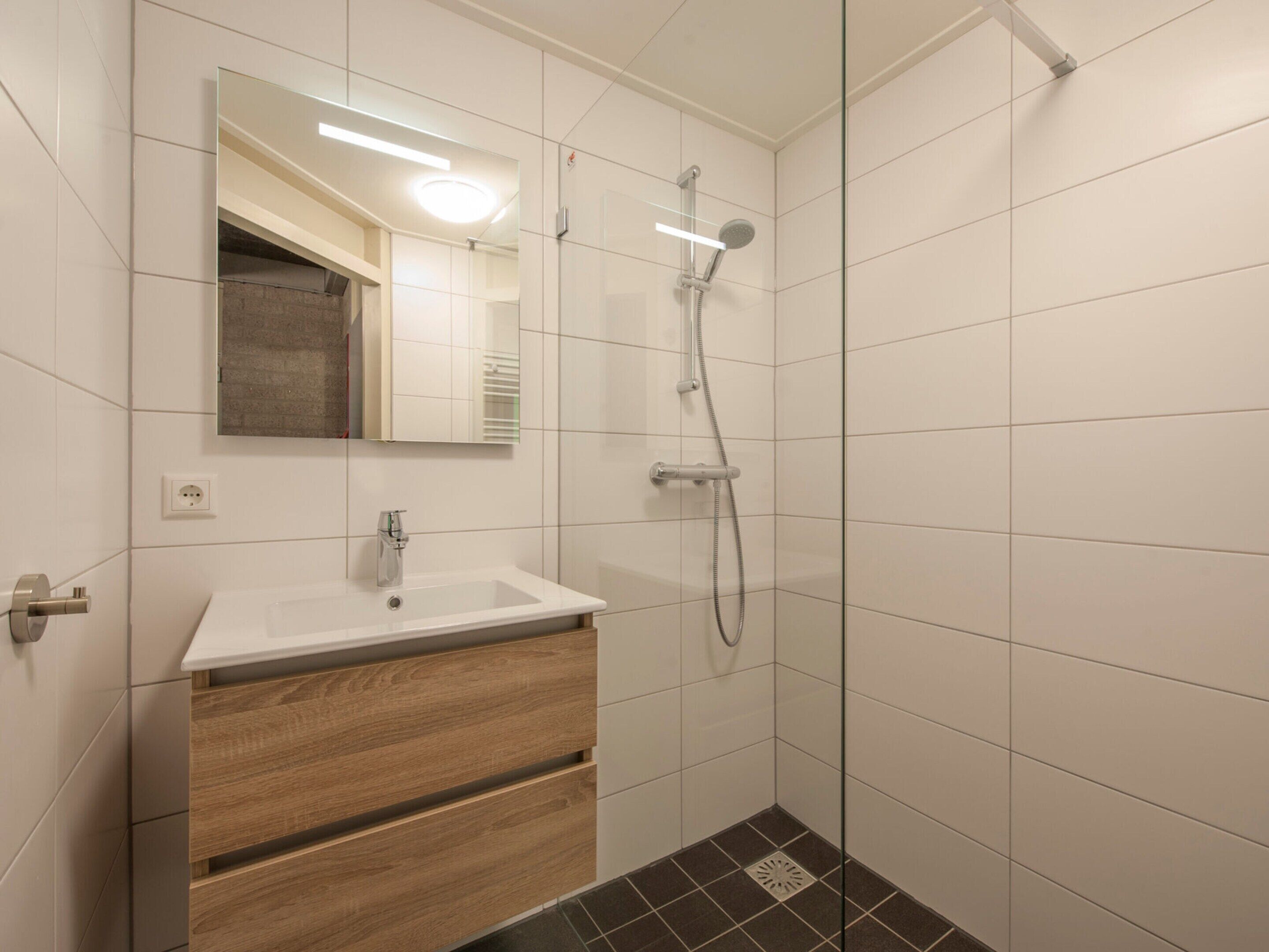 A modern bathroom with a white sink, wooden cabinet, and a glass shower enclosure.