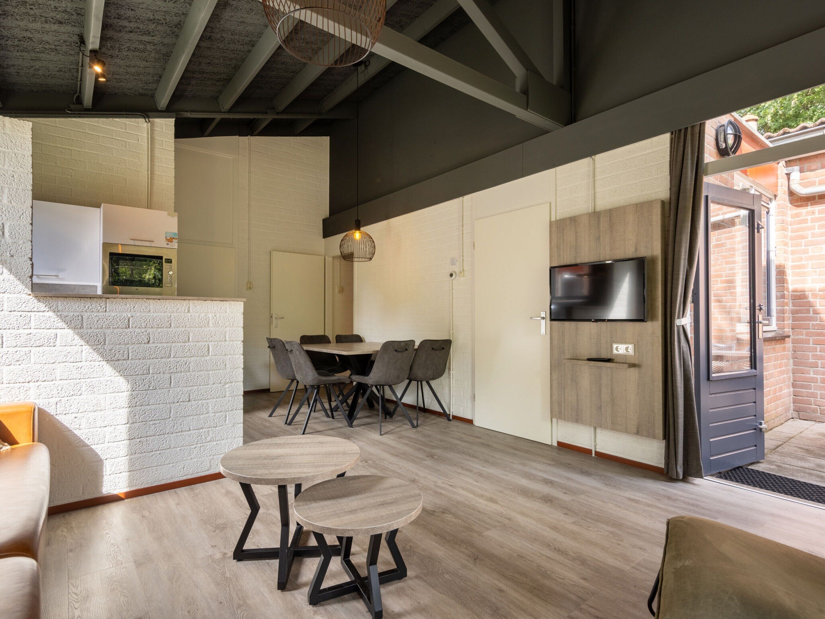 Eine moderne Küche mit eingebauter Mikrowelle, einem Essbereich mit rundem Tisch und Stühlen sowie einem an der Wand montierten Fernseher.
