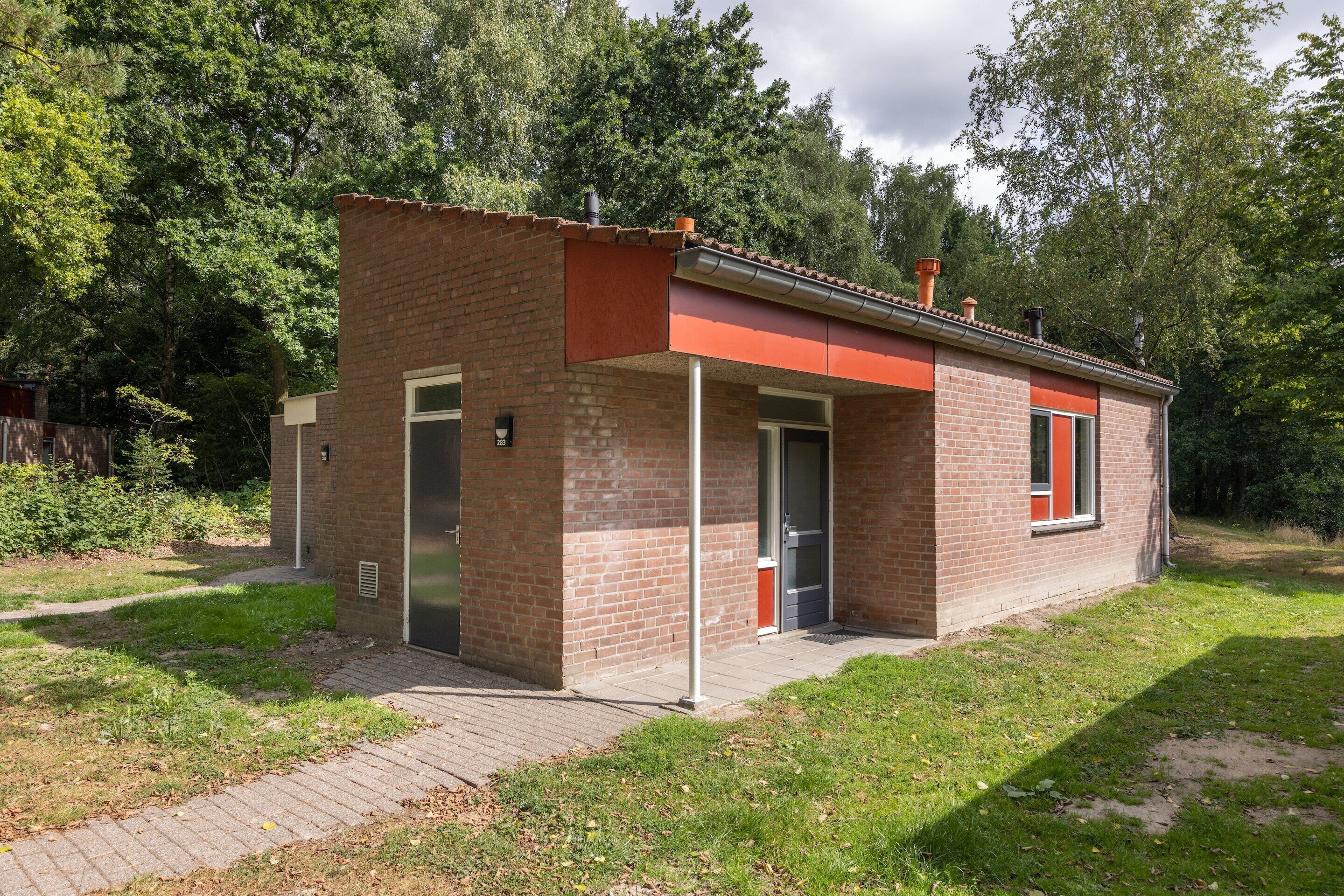 A small brick building with a red roof, a door, and a window.
