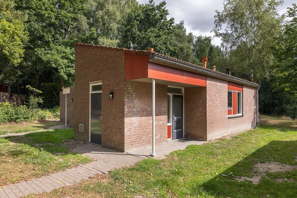 A small brick building with a red roof, a door, and a window.