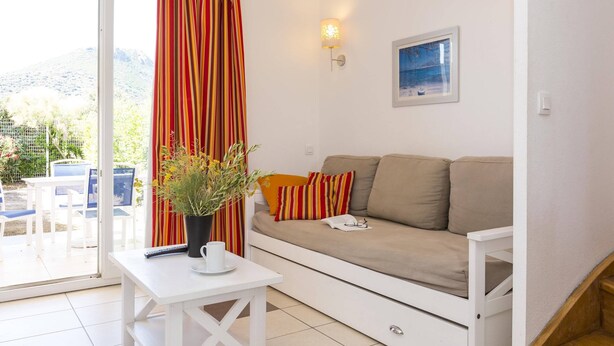 A living room with a sofa, a table with a plant, a remote control, and a picture on the wall. - Sea-view Holiday Home in Northern Corsica (Belgodere)