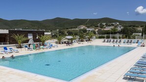 A swimming pool with lounge chairs, palm trees, and a view of hills and houses. - Sea-view Holiday Home in Northern Corsica (Belgodere)