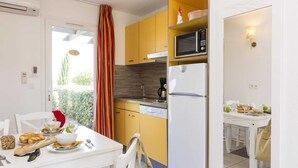 A compact kitchen with a microwave, refrigerator, and a dining area with a table set for two. - Sea-view Holiday Home in Northern Corsica (Belgodere)