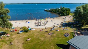 Ein Strand mit Volleyballnetz, Rasenflächen und Blick auf das Wasser.