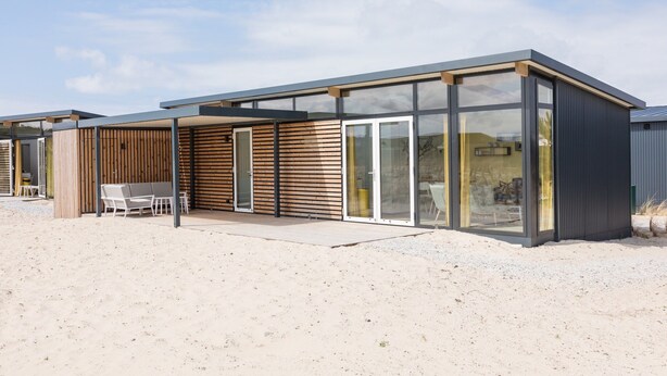Un bâtiment moderne doté d’un patio couvert, de grandes fenêtres et d’un sol sablonneux.