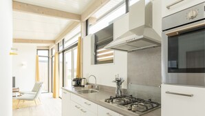 Moderni keittiö, jossa on valkoiset kaapit, ruostumattomasta teräksestä valmistetut kodinkoneet ja suuri ikkuna.