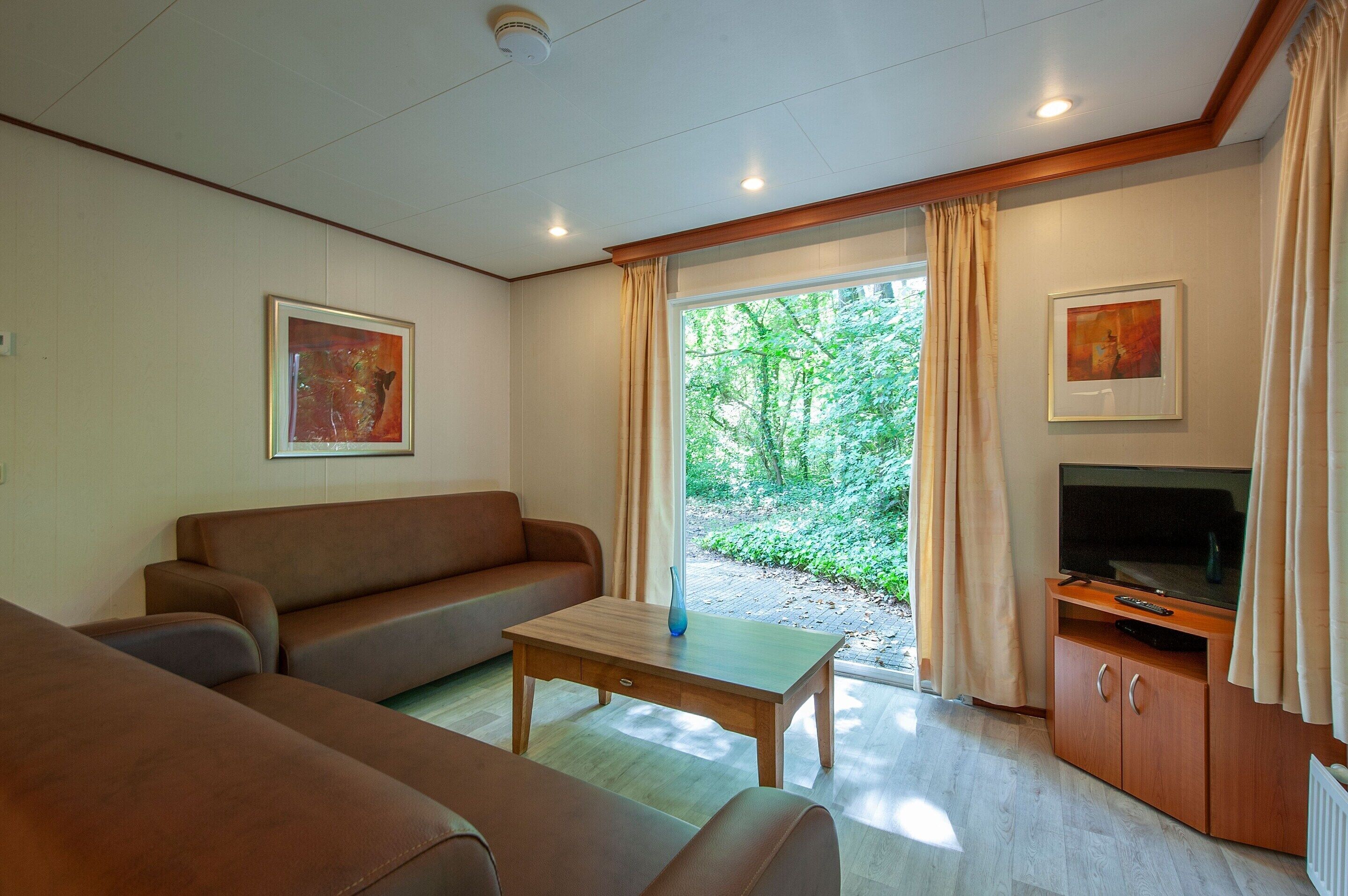 A living room with a sofa, a coffee table, a TV on a wooden stand, and a window with curtains.