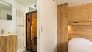 A modern bathroom with a glass shower enclosure, a wooden vanity, and a bed with a wooden headboard. - Wellness Stay With Sauna (Borger)