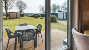 A patio with a table and chairs, a sliding glass door, and a view of a grassy area with buildings in the background. - Wellness Stay With Sauna (Borger)