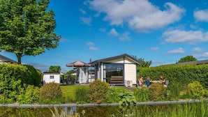 A modern house with a large glass window, a small attached garage, and a pond in the foreground. - Neat Chalet With Microwave Near the Beach in Egmond (Egmond aan den Hoef)
