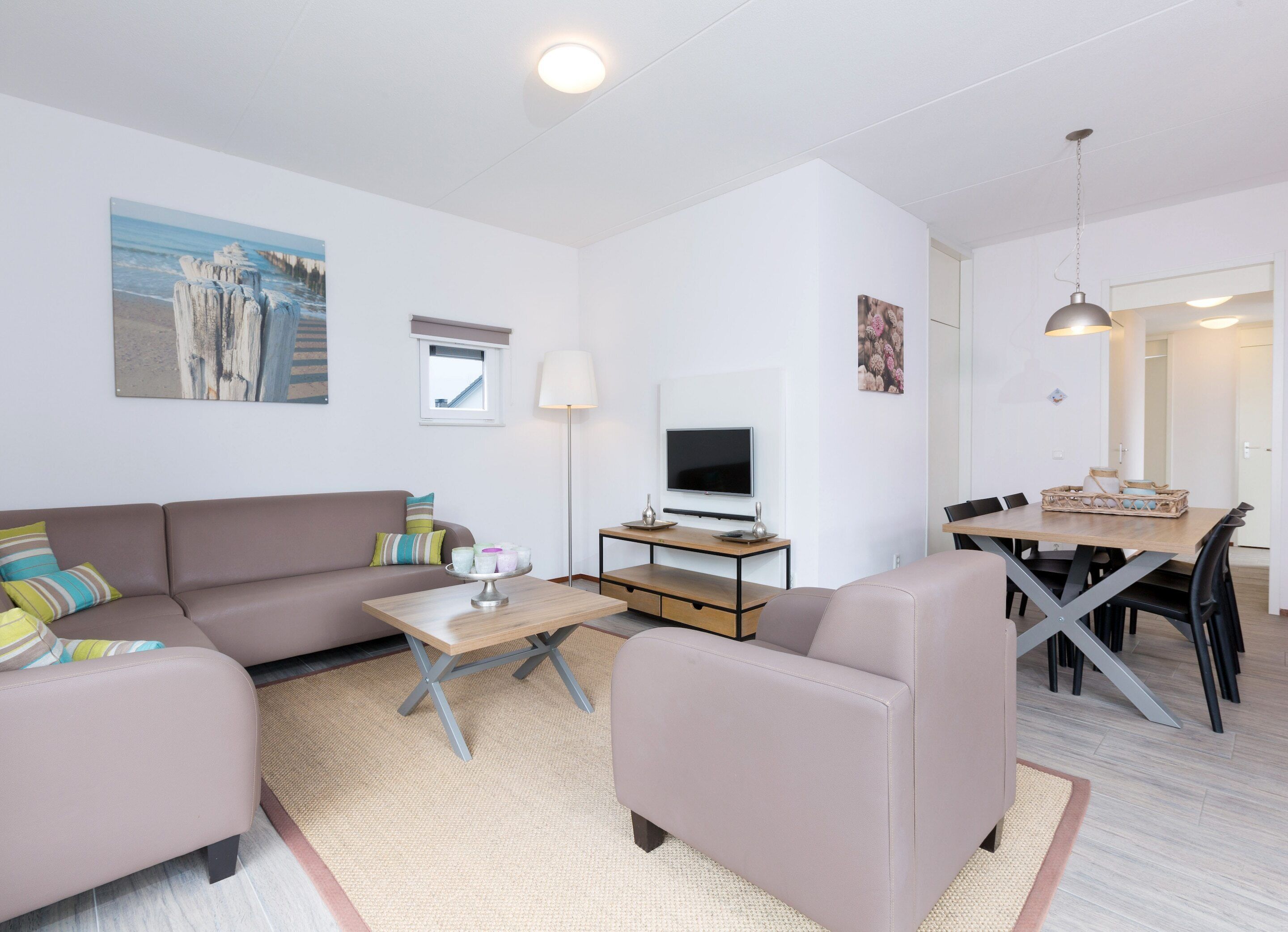 Una sala de estar moderna con un sofá, sillones, una mesa de centro, un televisor y un comedor con una mesa y sillas.