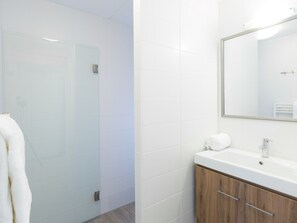 Een moderne badkamer met een glazen douchecabine, een houten wastafelmeubel met een spiegel, en een witte handdoek op de toonbank.