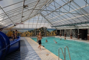 Una piscina interior con techo transparente, tobogán de agua y un mural en la pared.
