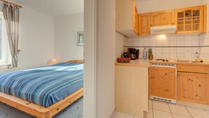 A bedroom with a bed and a kitchenette with wooden cabinets and a stove. - Ferienhaus mit Garten in Zingst (Zingst)