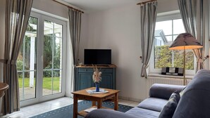 A living room with a sofa, a wooden coffee table, a TV on a blue cabinet, and a lamp. - Ferienhaus mit Garten in Zingst (Zingst)