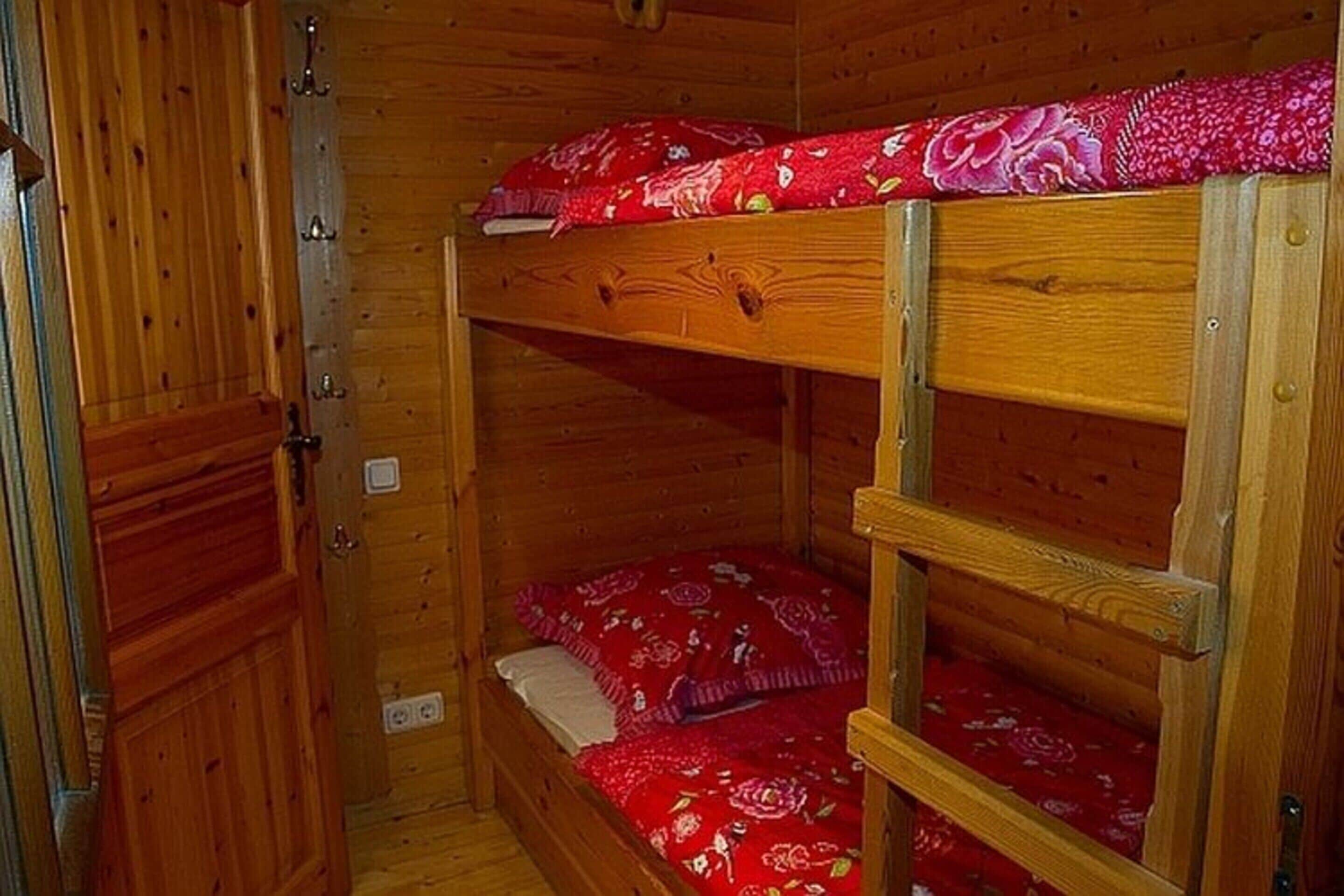 Ein Zimmer mit einem hölzernen Etagenbett und einer roten Bettdecke mit Muster.