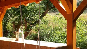 A wooden swing with ropes, a white lantern, and a view of greenery.