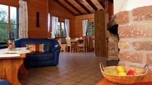 A wooden interior with a blue sofa, dining table, and a stone fireplace.