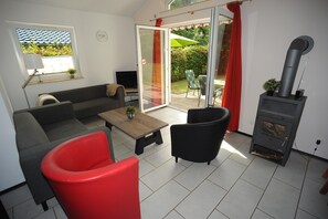 A living room with a sofa, a red chair, a television, and a fireplace. - Bungalow Near Eifel Ski Lift (Gerolstein)
