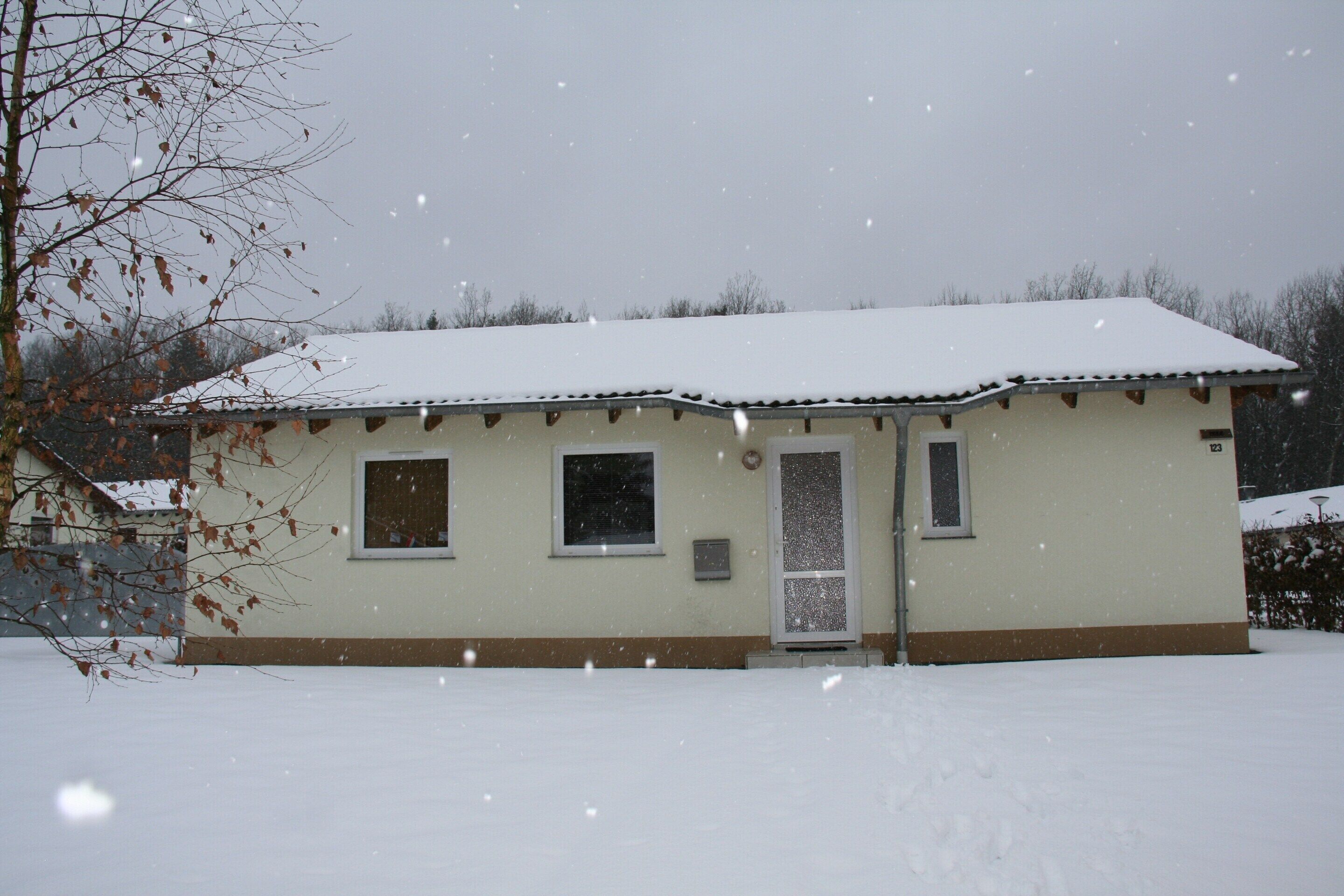 Een huis met één verdieping, met een met sneeuw bedekte sneeuw en een voordeur.