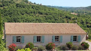 A single-story building with a tiled roof, surrounded by lush greenery and hills. - Villa Near Les Vans Centre (Les Vans)