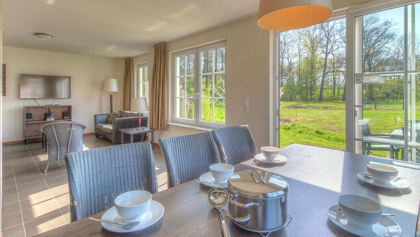 A dining area with a table set for four, a television, and a view of a garden.