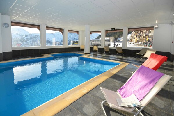 En indendørs swimmingpool med frit udsyn til bjerge, liggestole og et fliset gulv.