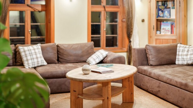 A cozy living room with a brown leather sofa, a wooden coffee table, and a bookshelf.