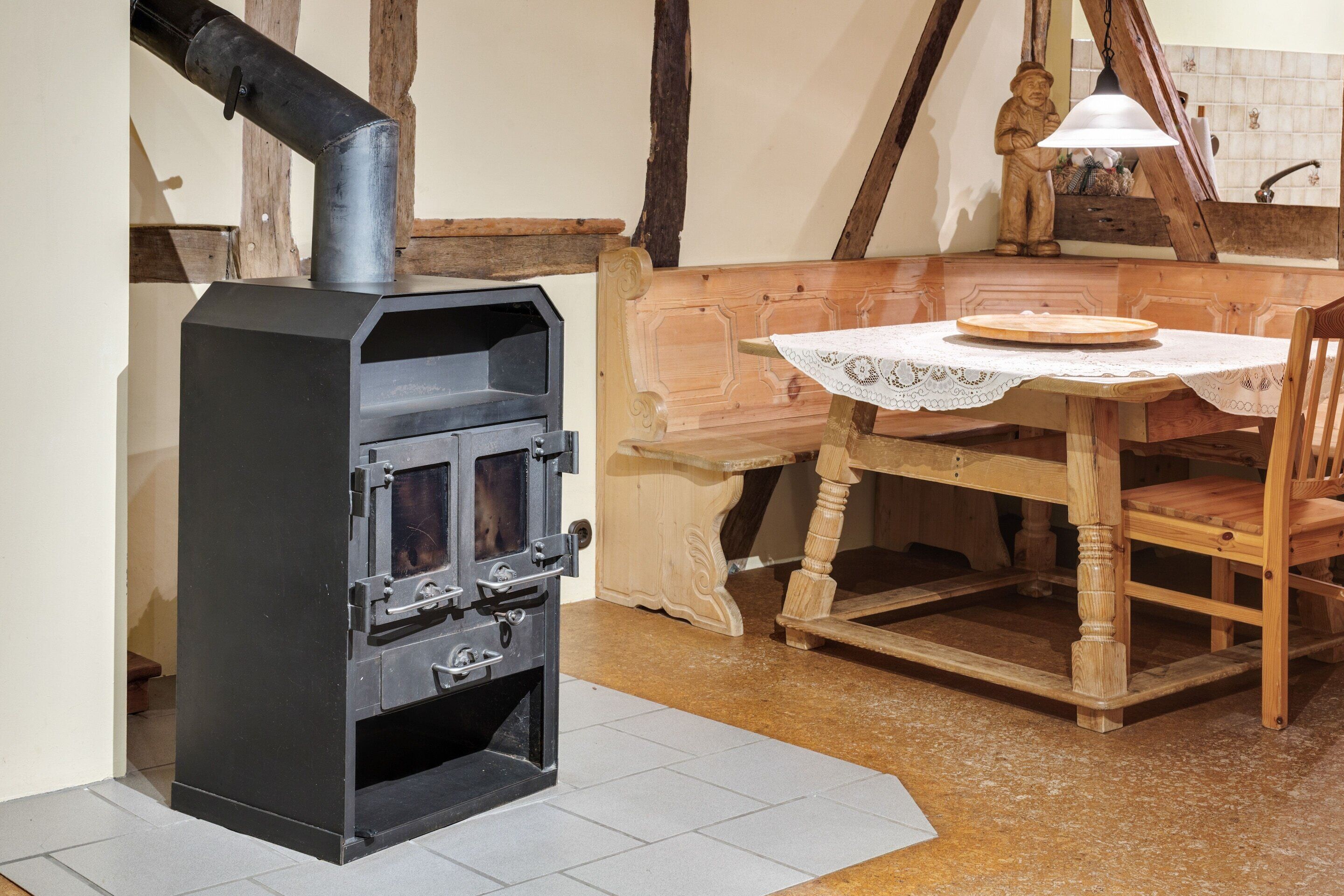 Ein traditioneller Holzofen, ein Holztisch mit Stühlen und eine rustikale Holzbank.