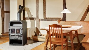 A cozy room with a wood-burning stove, a wooden table with a lace tablecloth, and a bench.