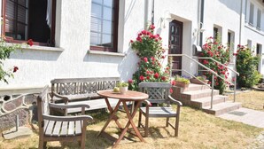 Une terrasse avec une table et des chaises en bois, un mur en pierre et un escalier menant à une porte.