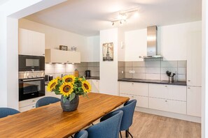 Eine moderne Küche mit weißen Schränken, einem eingebauten Backofen und einem Essbereich mit einem Holztisch und blauen Stühlen.