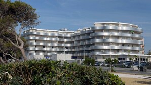 Un edificio de varios pisos con balcones, un estacionamiento y un árbol en primer plano.