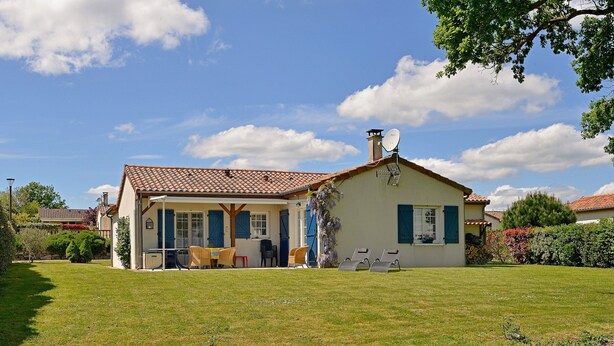 Une maison avec un toit en tuiles, un patio couvert avec des chaises et une pelouse bien entretenue.