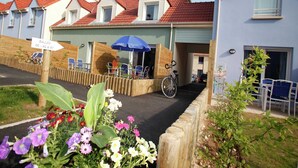 A row of houses with red-tiled roofs, a covered outdoor seating area with a blue umbrella, and a bicycle parked outside. - Spacious Coastal Apt w/ Garden (Le Crotoy)