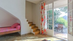 Une pièce avec un escalier, un canapé agrémenté d’un coussin rose, une table rouge et une fenêtre donnant sur un paysage verdoyant.
