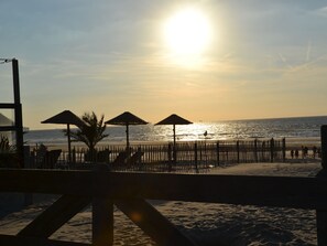 Ein Strand mit Sonnenschirmen und Liegestühlen, eine Holzlattenveranda und Blick auf den Ozean.