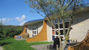 A building with a curved facade, a patio with outdoor furniture, and a tree in the foreground. - Bungalow in South Holland With Unique Design ('s-Gravenzande)