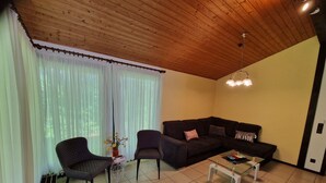A living room with a wooden ceiling, a dark-colored sofa with cushions, two armchairs, a coffee table, and a floor lamp. - Holiday Home in Germany With Idyllic Nature (Ronshausen)