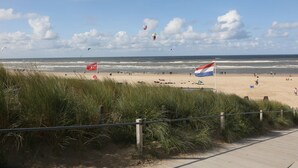 A beach with flags, a boardwalk, and the ocean.