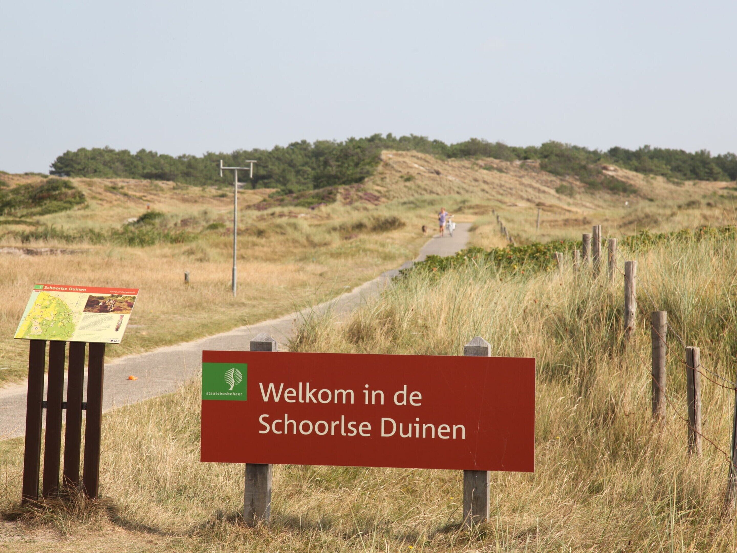A welcome sign in Dutch at the entrance to a natural area, with a map and informational leaflet on a stand.